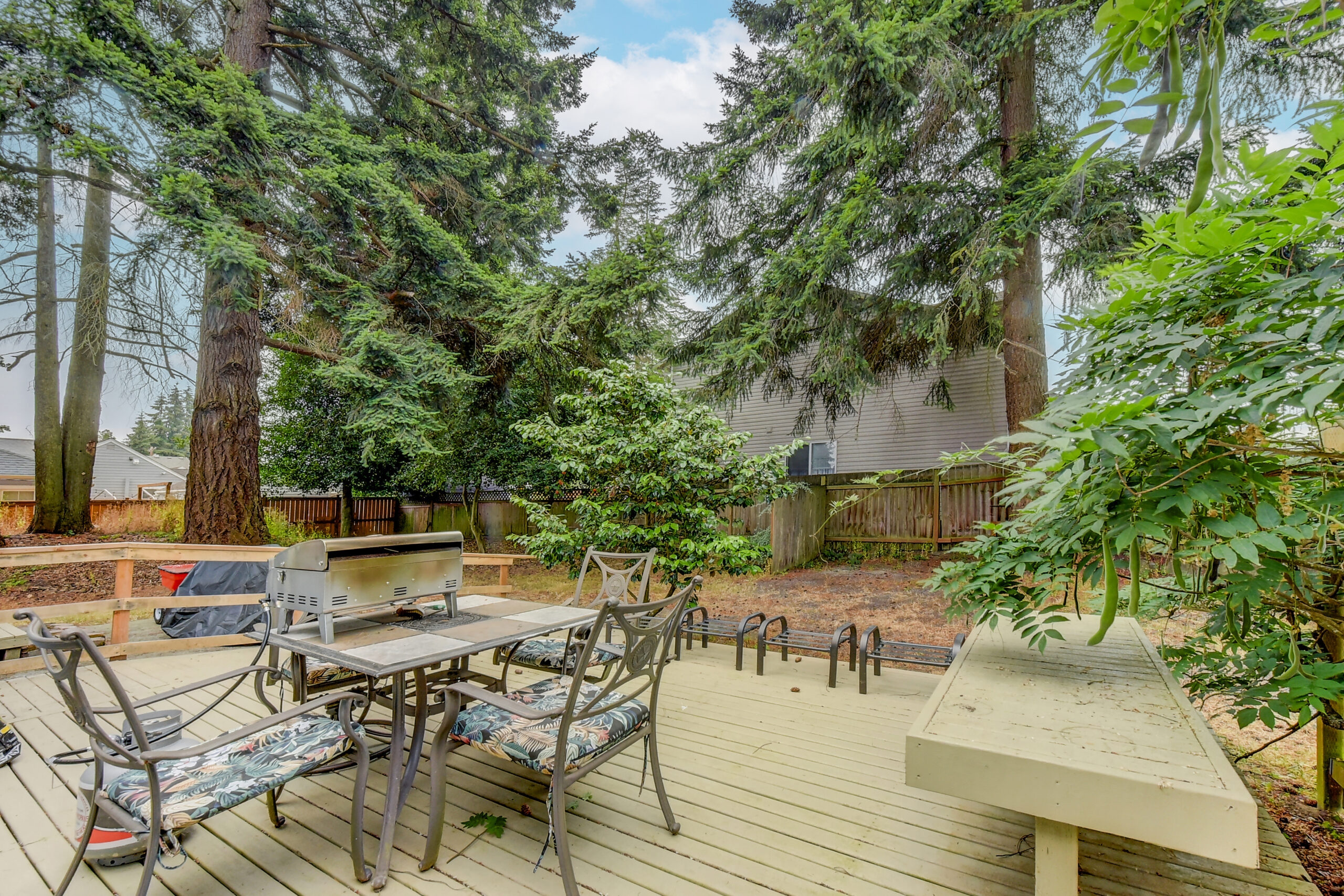 Backyard deck with patio seating and grill, surrounded by tall trees and fenced yard, Everett home