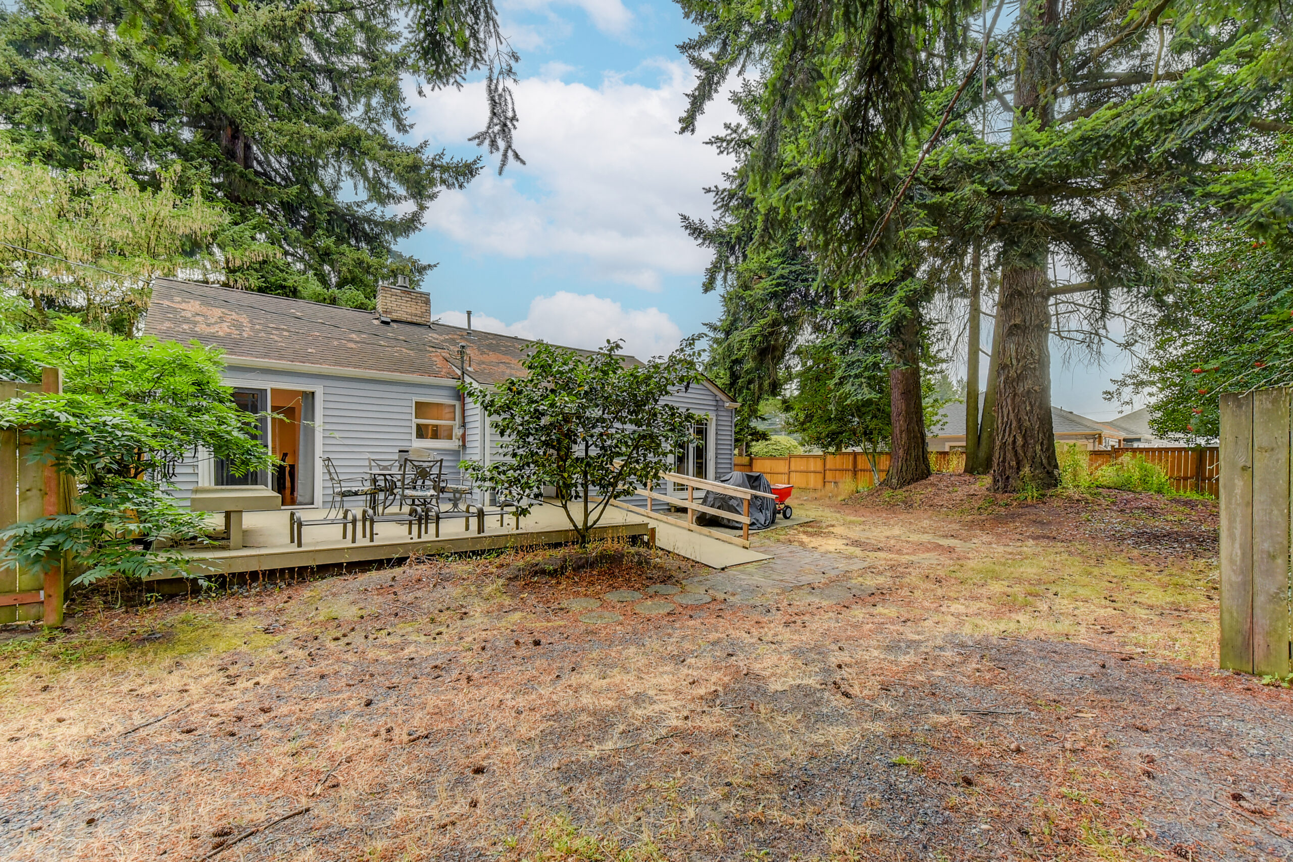 Backyard of the Everett rambler with deck, ramp, and fenced quarter-acre lot lined with tall trees