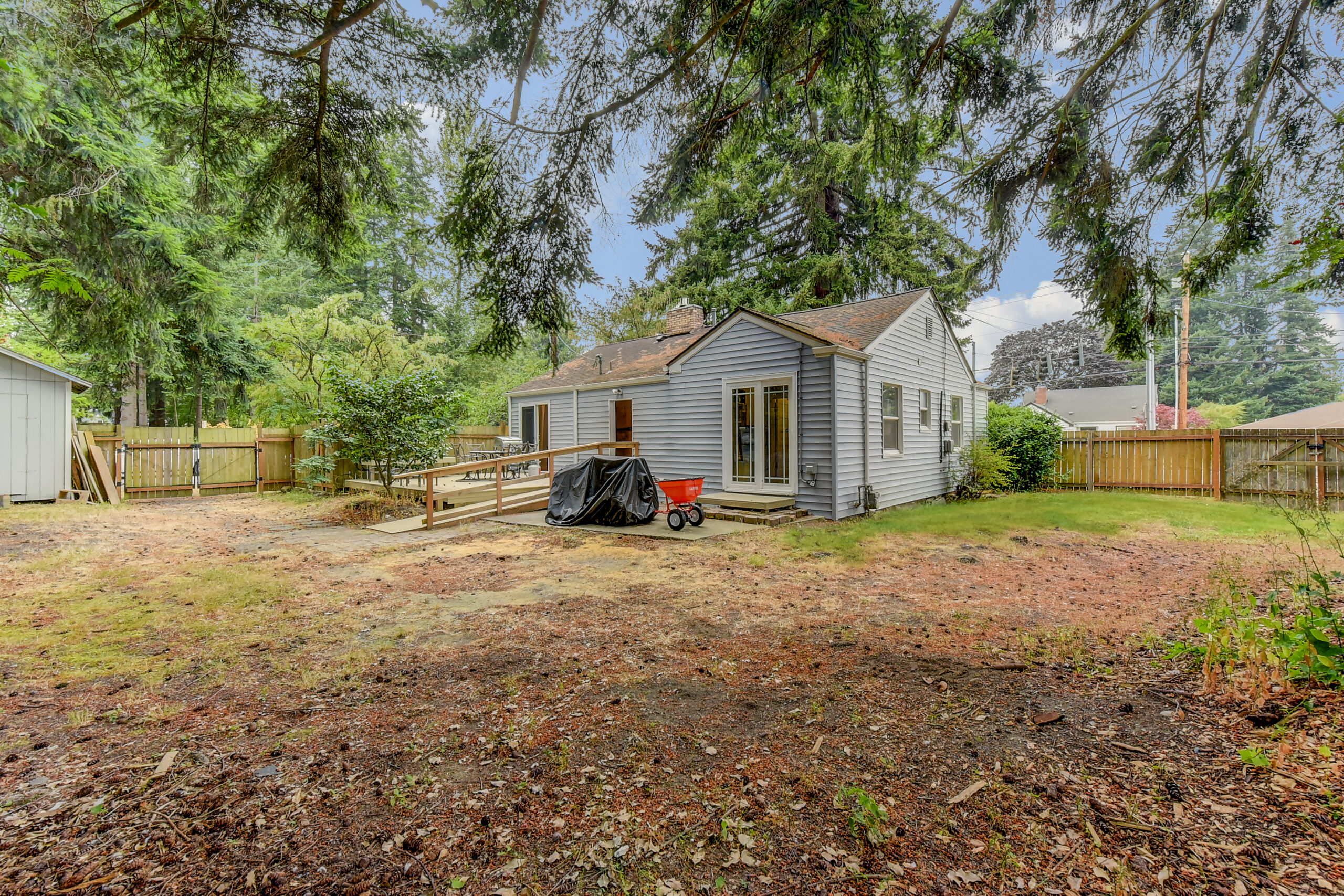 Fenced backyard of the Everett rambler, with deck ramp, garden shed, and mature trees