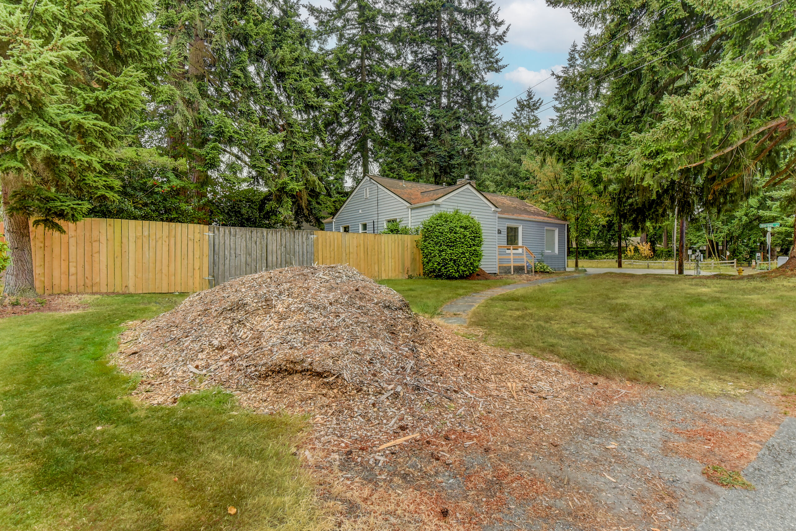 Fenced backyard and lawn of the Everett rambler, with mulch pile, trees, and rear exterior view