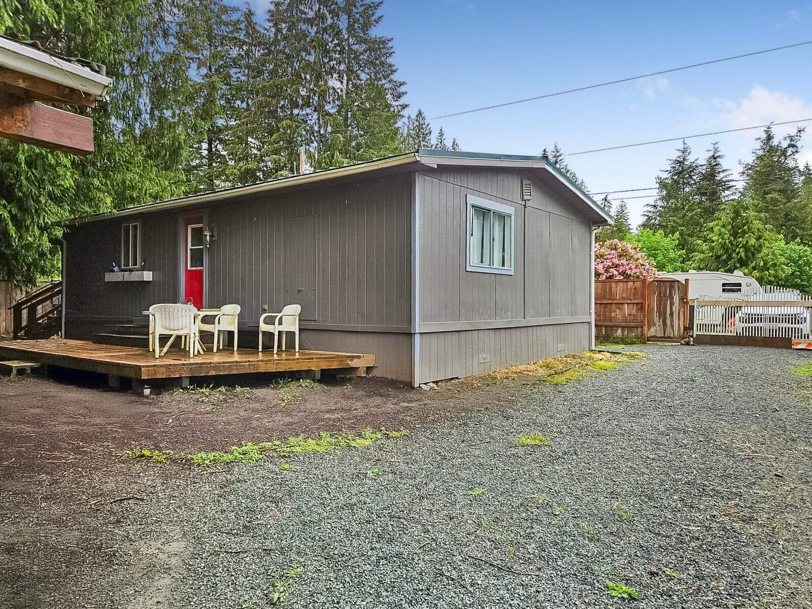 Exterior of the Concrete manufactured home with red door, front deck seating, and gravel driveway