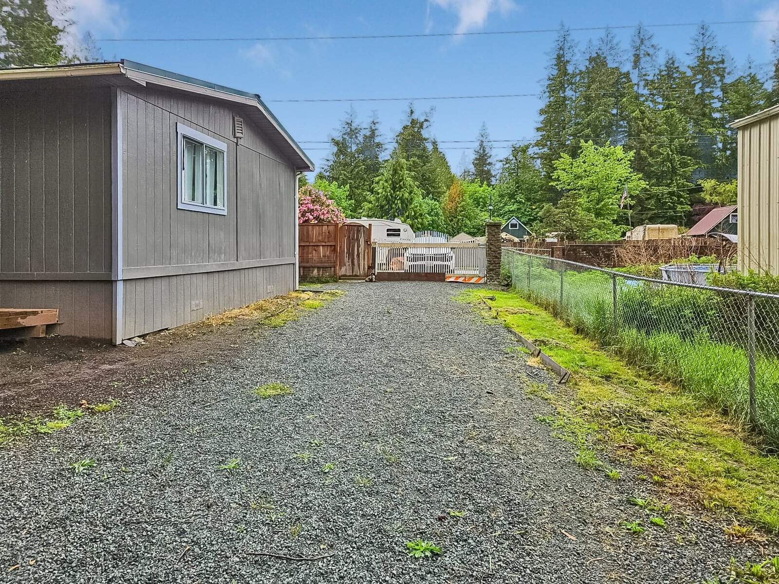 Gravel driveway along fenced side yard leading to gated entrance, Concrete home