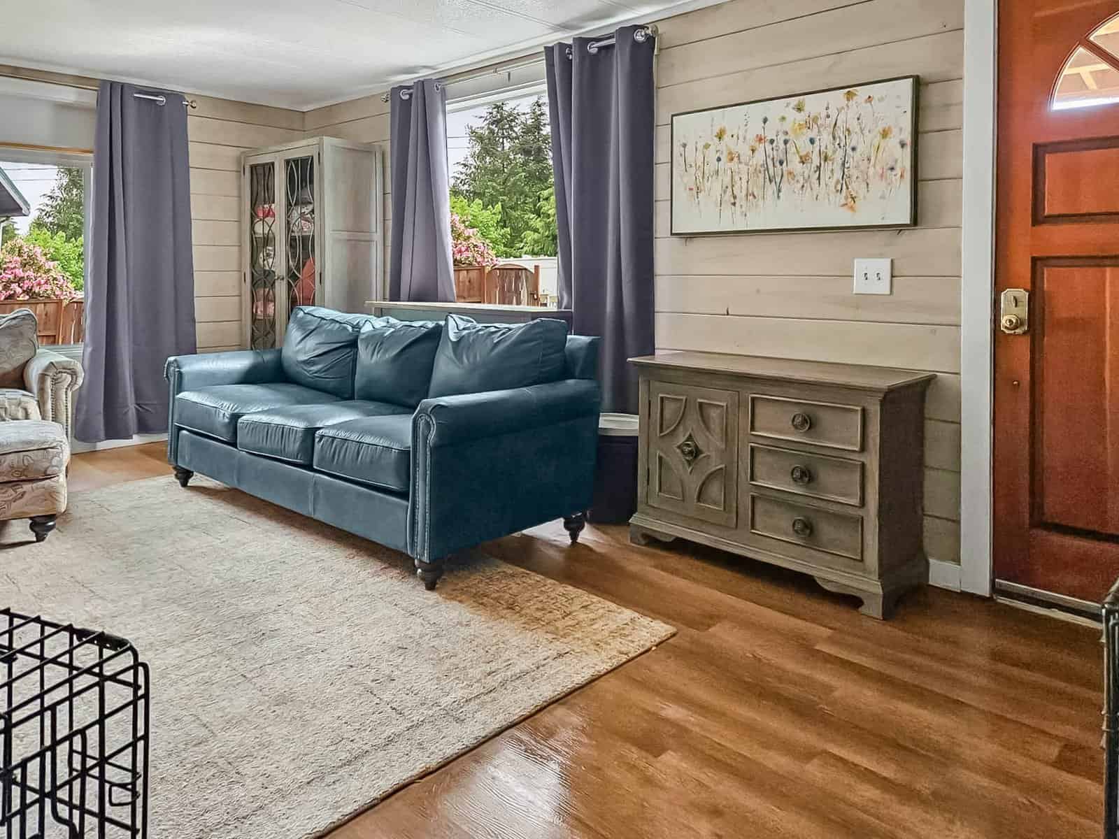 Living room with leather sofa, wood floors, and shiplap walls at Concrete home for rent-to-own