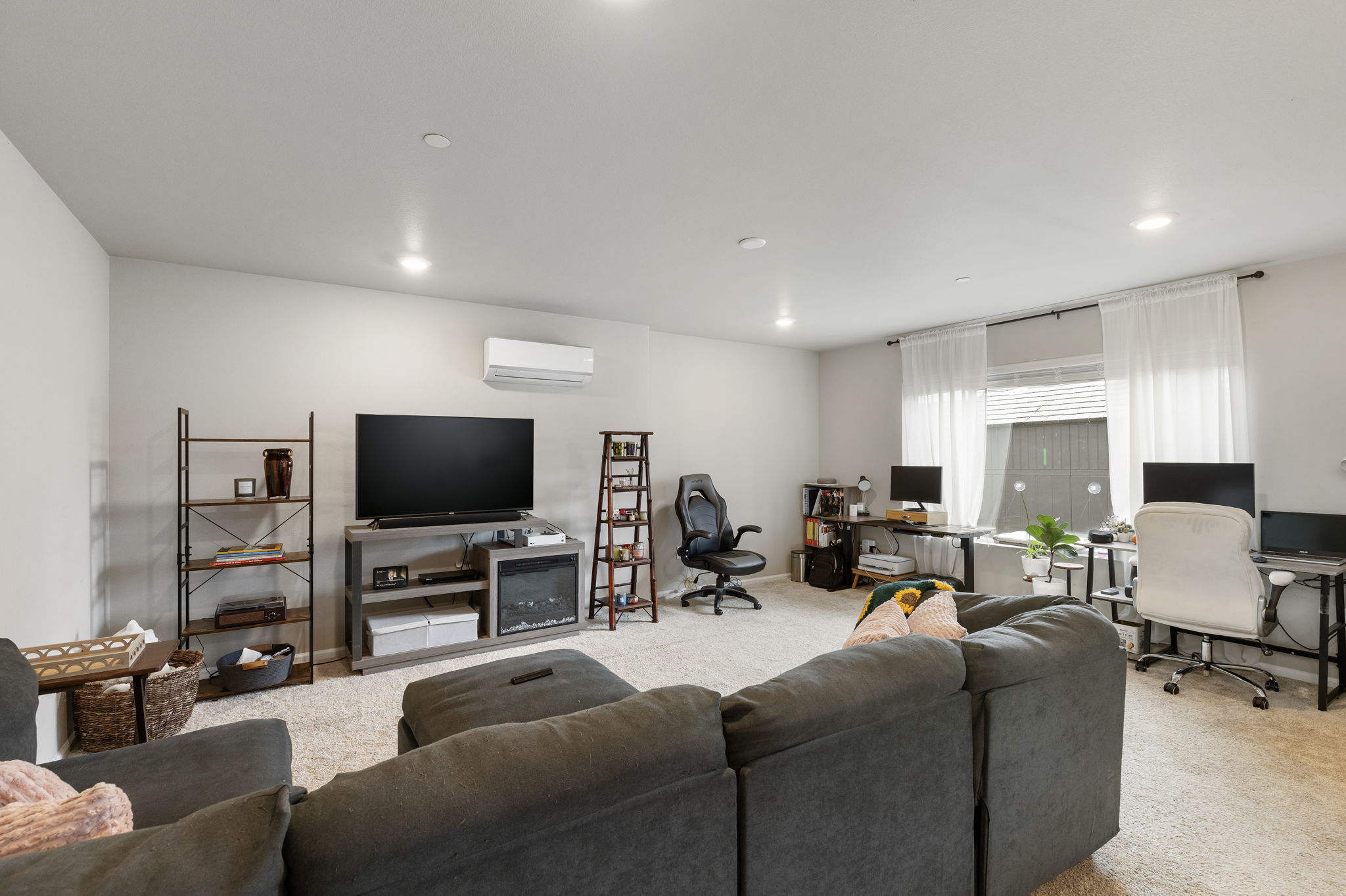 Basement family room with sectional, TV, and dual desk setups in the Port Orchard rent-to-own home