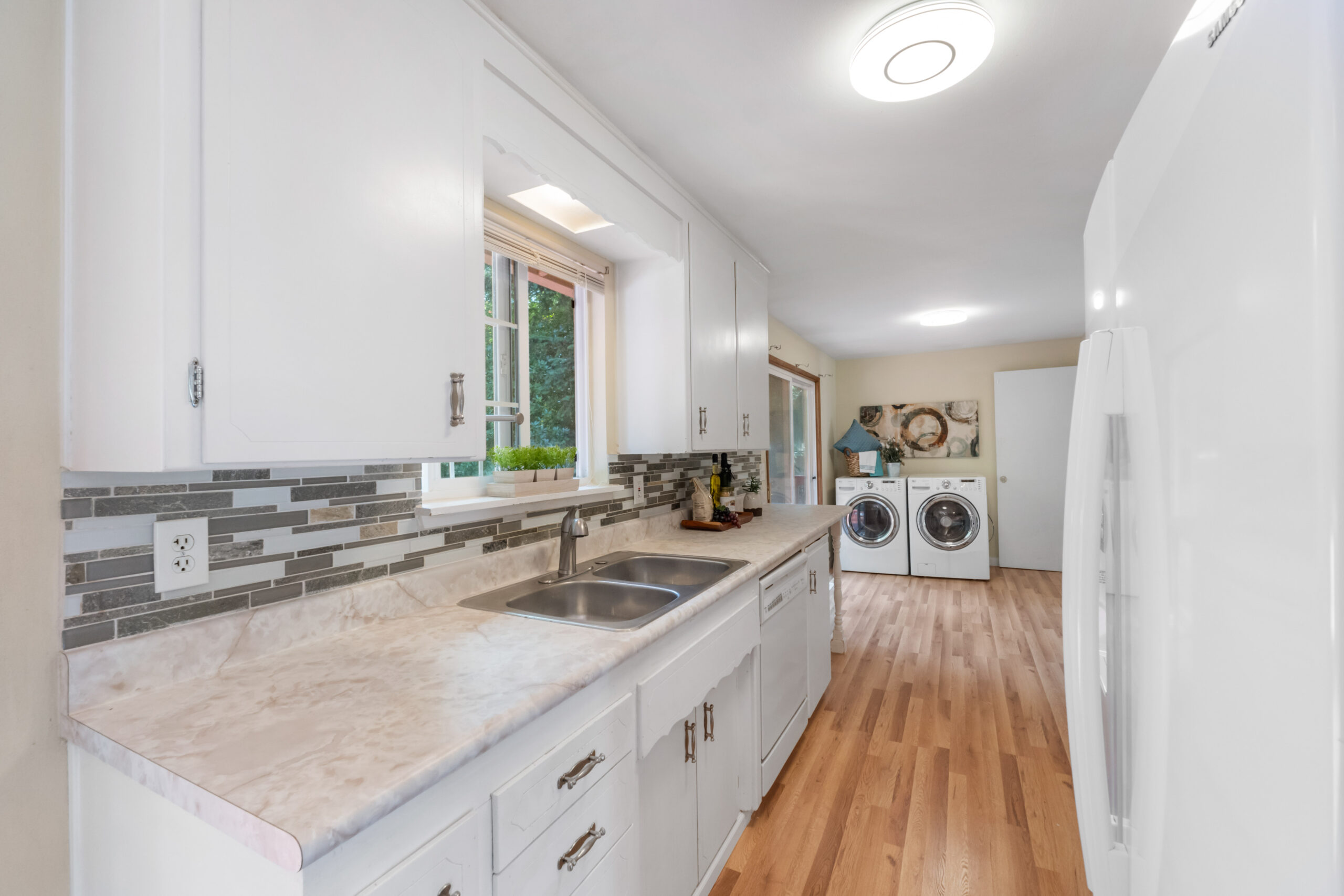 Kitchen with white cabinets and tile backsplash opening to laundry area, Auburn duplex unit