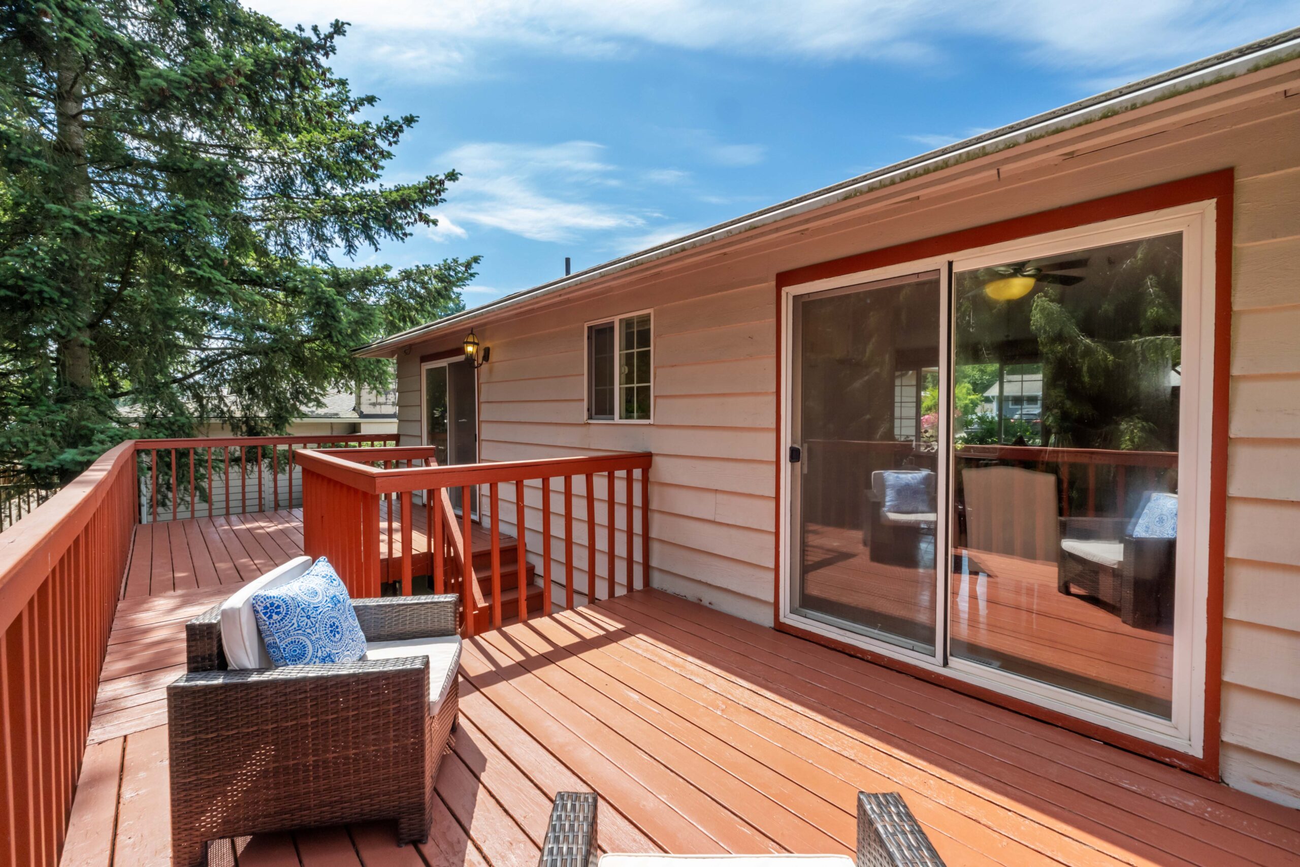 Large deck with wicker seating off the upstairs unit at the Auburn duplex, shaded by tall trees